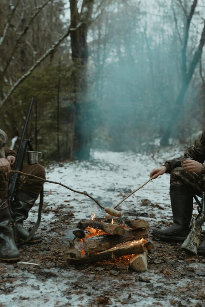 Two hunters roasting marshmallows near a campfire in a snowy forest.